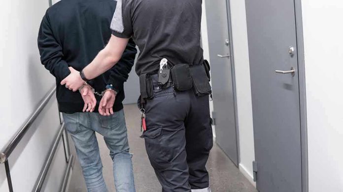 1082126789 Officer escorting handcuffed person down hallway