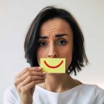 Woman holding a smiley face sticky note.