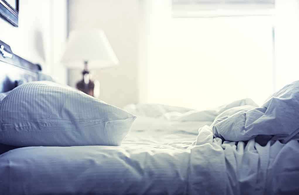 A cozy unmade bed with soft pillows and bedding in a well lit room