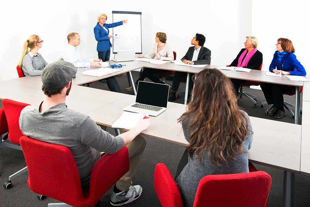 A diverse group of professionals engaged in a meeting with a presenter at a whiteboard