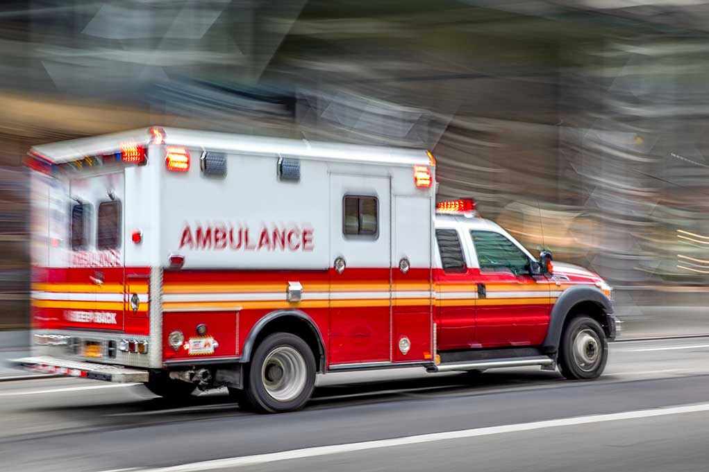 1495131698 Red and white ambulance driving on street.