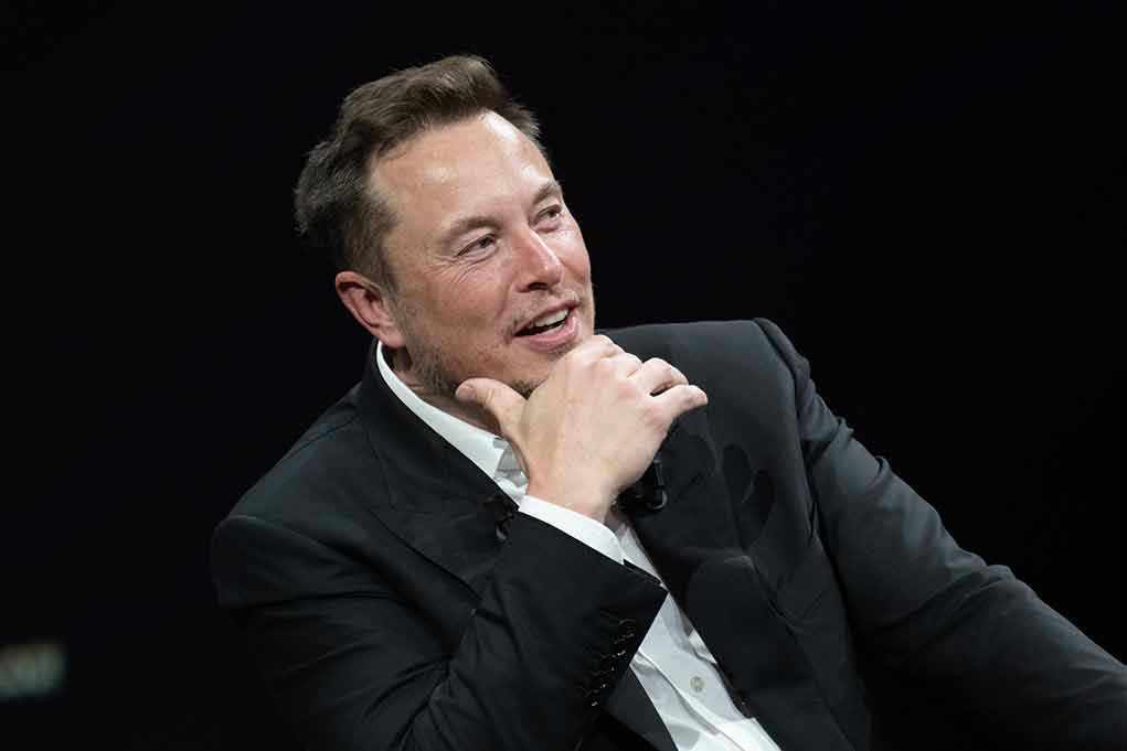 2318800327 Man in suit smiling, resting chin on hand.