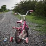 Britain’s 2,000 Missing Kids – Government Scrambles Pink childrens bike with training wheels on gravel path.