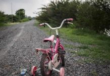 Britain’s 2,000 Missing Kids – Government Scrambles Pink childrens bike with training wheels on gravel path.