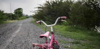 Pink childrens bike with training wheels on gravel path.