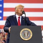 Trump Lifts Restrictions – Ignites Oil FRENZY! Man speaks at podium with U.S. flag background.