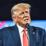 Autopen Presidency EXPOSED – Trump CANCELS ALL! Man in suit speaking at a microphone.