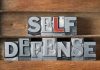 Metallic block letters spelling SELF DEFENSE on wooden shelves.