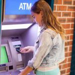 $124 Trillion Up for Grabs—Who Gets Left Out? Young woman using an ATM in an urban environment