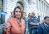 Trump UNLEASHES “Evil” Bomb on Pelosi Exit A woman in an orange blazer speaking passionately at a rally with security personnel in the background