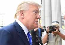 Trump’s Explosive Somali Remarks Ignite Fury Man in suit with photographers in background.