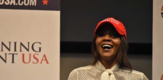 A woman wearing a red cap and a white blouse speaking at a political event
