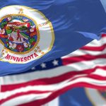 Minnesota state flag with American flag in background.
