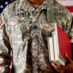 A soldier in a U.S. Army uniform holding books in front of an American flag