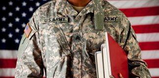 A soldier in a U.S. Army uniform holding books in front of an American flag