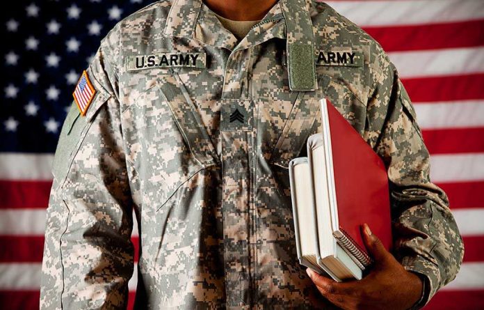 A soldier in a U.S. Army uniform holding books in front of an American flag
