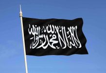 Islamic State FALLS APART – Mullah FLEES to RUSSIA! Black flag featuring Arabic script against a blue sky