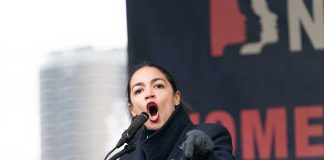 Woman speaking passionately at podium during outdoor event.