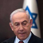 Netanyahu Hospitalized – Cancer Rumors Circulate Man in suit with Israeli flag in background.