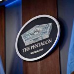 Pentagon Hire’s J6 Rioter Sparking Firestorm! The Pentagon emblem between two flags.