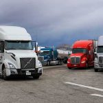 Semi trucks parked at a rest area under cloudy sky
