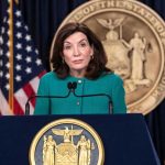 Governor CAUGHT! Paying Cops to Shield Illegals! Kathy Hochul speaks at podium with New York State emblem.