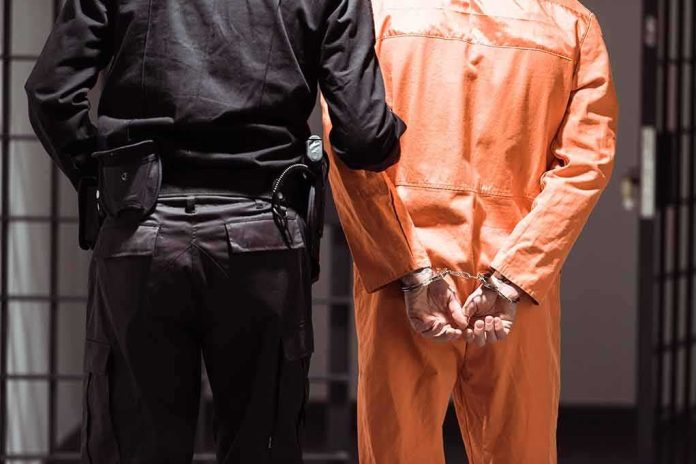 shutterstock_1030213828 Prisoner in orange jumpsuit handcuffed with guard standing beside