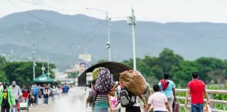 People walking across a bridge carrying bags and bundles