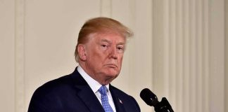 $38B And Climbing: Iran War BANKRUPTING U.S man in suit at a podium