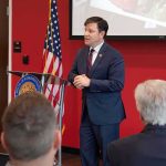 Missing Congressman’s Father BREAKS SILENCE Speaker in a navy suit addressing an audience at a podium