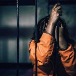 Prisoner in orange jumpsuit gripping jail bars