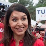 Tulsi Gabbard smiling at an outdoor event surrounded by supporters