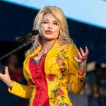 Disturbing Details Emerge Of Dolly Parton’s Final Hours Dolly Parton performing on stage in a yellow floral jacket