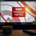 World Cup Fans DENIED Visa’s – Get Free T.V’s Instead! Television displaying world news program with cup and remote in foreground
