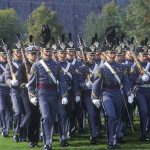 Cadets in dress uniforms marching in formation with rifles