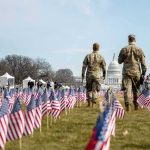 Two soldiers walk among American flags toward the U.S. Capitol