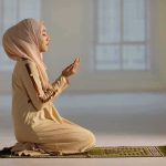 Woman in hijab praying on a mat indoors