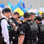 Suspect ARRESTED After Erika Kirk Bomb Threat! Police officers stand among a crowd with blue and yellow flags