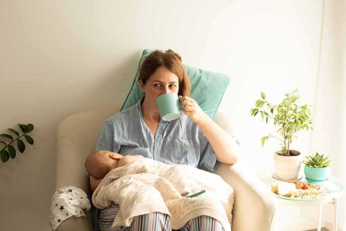 shutterstock_2135823883 Mother nursing baby while drinking from a mug in a cozy chair