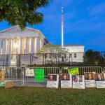 Protestors SWARM FBI Director During Funeral Supreme Court building behind fences and protest signs at dusk