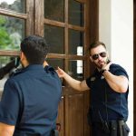 Pizza Standoff Ignites – Servicemen DENIED! Two police officers check a wooden door with glass panels
