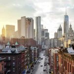 City street leading to a skyline of modern and historic skyscrapers at sunset