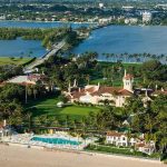 Aerial view of a waterfront estate with pool, lawns, and palm trees