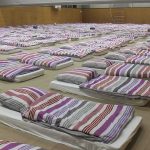 25 DEAD, 100 Injured in Prison BLOODBATH! rows of mattresses with striped bedding in a large hall