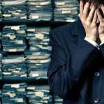 Pentagon Slashes 180 I.D’s From List! Man in suit covering face beside stacks of paperwork
