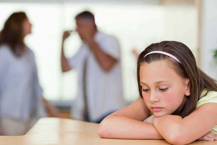 Sad girl resting her head on arms with blurred adults arguing in background
