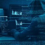 Hooded person at multiple computer screens with code and charts