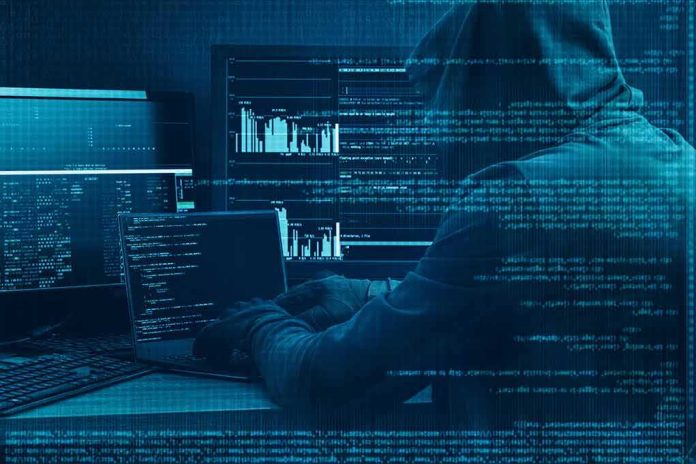 Hooded person at multiple computer screens with code and charts