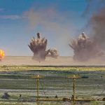 Multiple explosions erupt on a distant desert plain